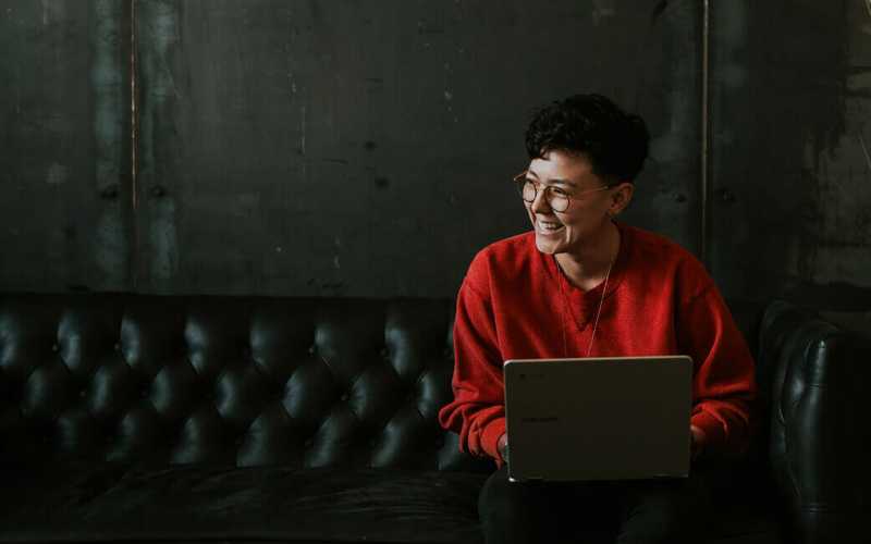 A woman sitting on a couch with a laptop in her lap smiling to someone
